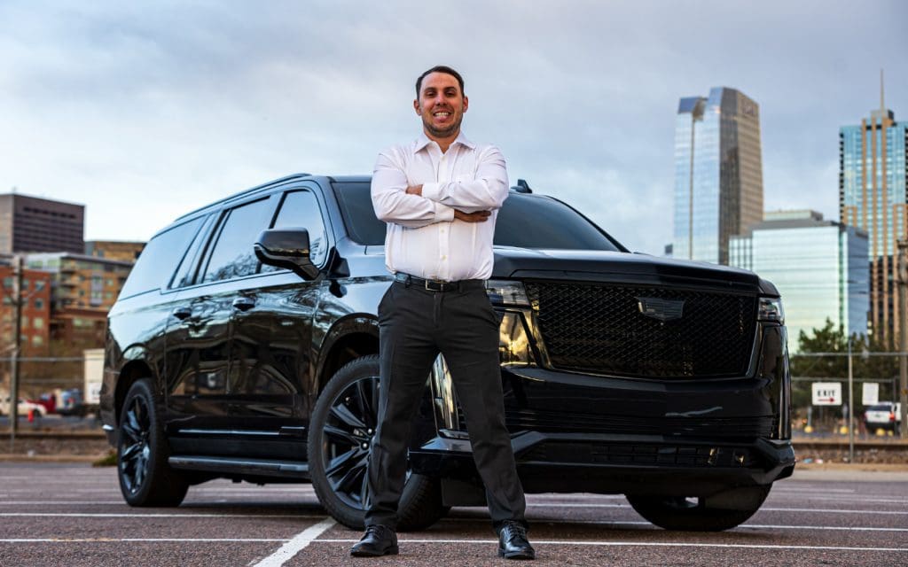 Chauffeur standing beside a black SUV, the private chauffeur service Mile High Chauffeur runs in Denver