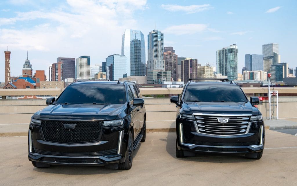 Black SUVs parked with the downtown Denver skyline behind them before an Empower Field event